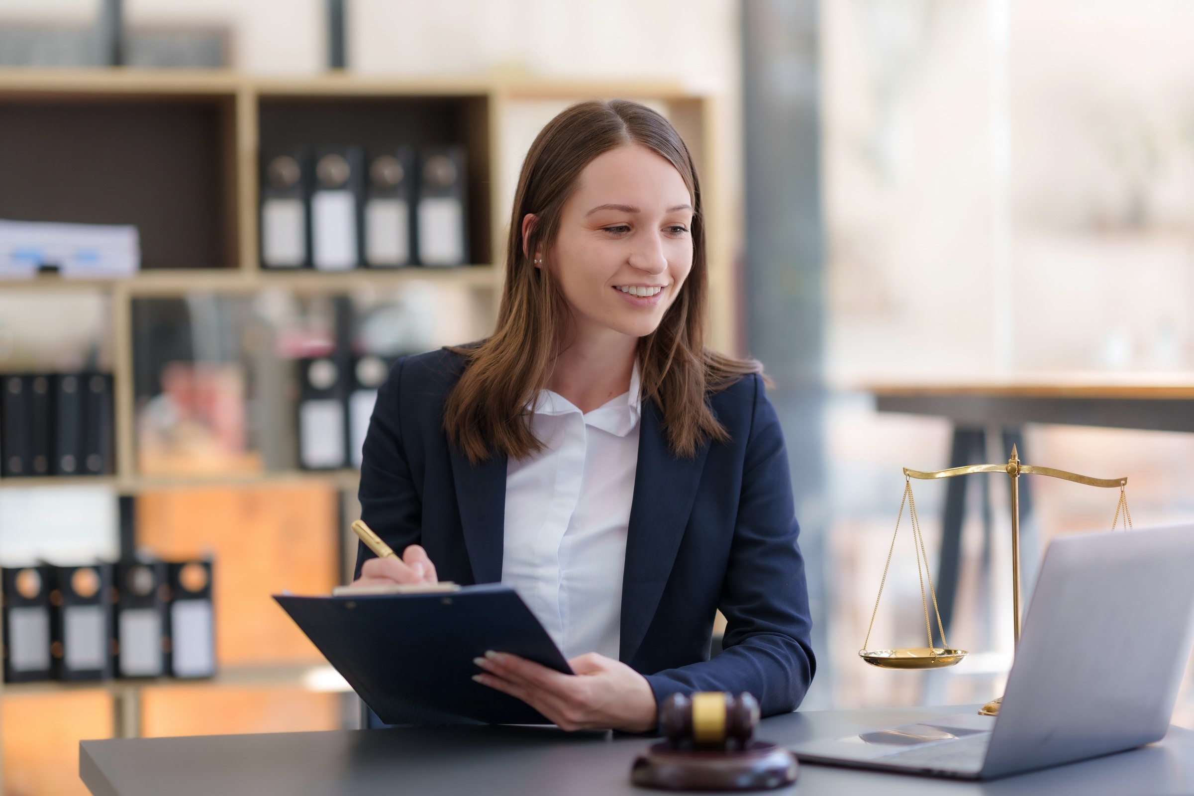 Female lawyer sitting happily working on laptop computer with hammer and legal book scales.